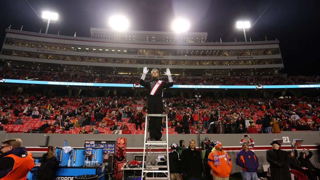 Thomas Peters standing on a ladder above the band in crowded Carter-Finley Stadium