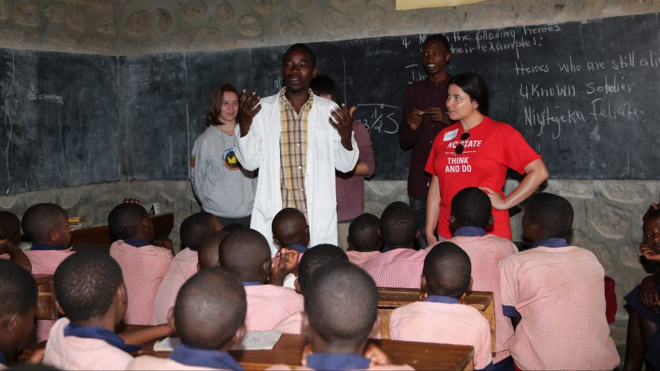 Esmira in front of a classroom of students in Rwanda, joined by a teacher